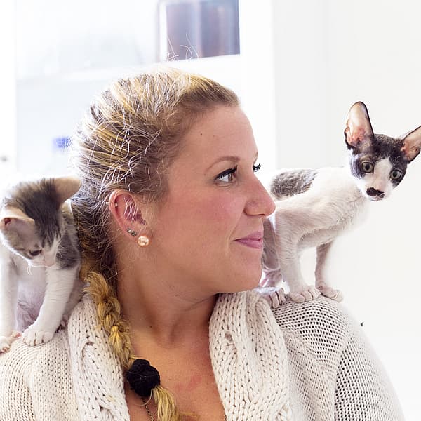 Två svartvita katter sitter på en blond kvinnas axlar.