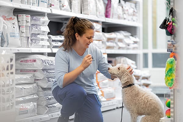 Kvinna klappar på en vit hund. Kvinnan och hunden står i en butik bland hundfoder och hundleksaker.